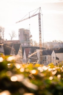 A construction crane towers over a building site against the backdrop of old half-timbered houses,