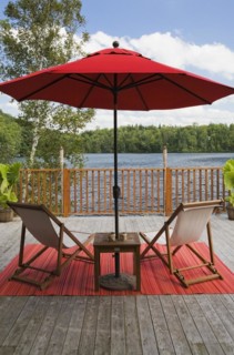 Red canvas cloth parasol and wooden folding canvas chairs on red mat on grey wood plank deck with