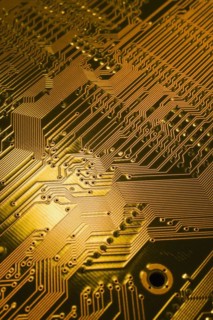 Close-up of golden yellow lighted electronic computer circuit board with lines and silver solder