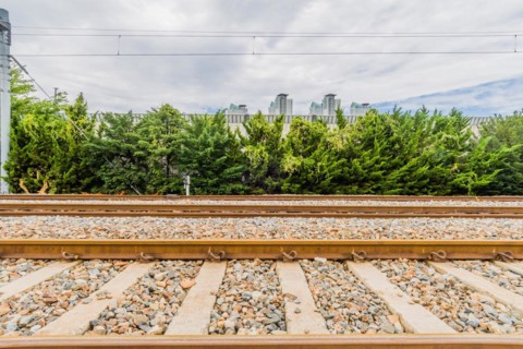 Railway tracks on a bright day with lush green foliage and city buildings under a sky with fluffy