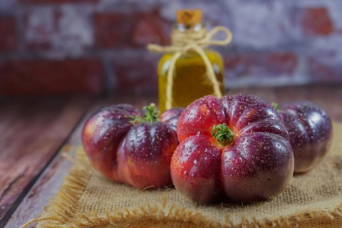 Group of tasty fresh tomatoes of the blue variety on a burlap cloth with a bottle of olive oil in