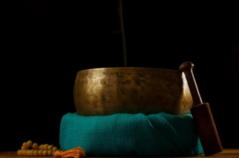Tibetan singing bowl smoking on green cloth next to a Buddhist japa mala isolated on black