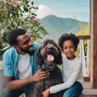 A man and a little girl are posing with a dog. The dog is wagging its tail and the girl is smiling.