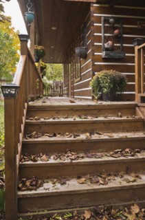 Old brown stained wooden stairs and long veranda with pine wood rocking chair and fallen tree