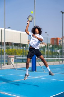 Vertical full length photo of a african american young sportive man jumping to reach the ball