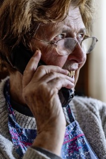 Laughing senior citizen with smock talking on the phone at home in her living room, Cologne, North