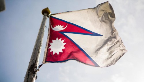 The flag of Nepal, fluttering in the wind, isolated against a blue sky