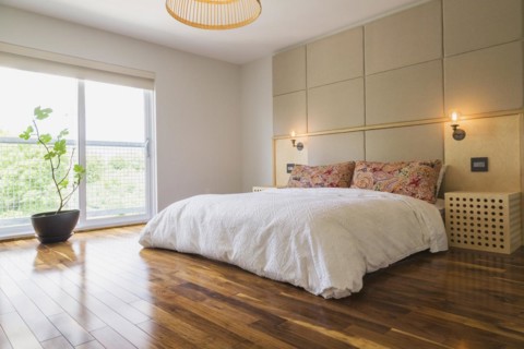 King size bed covered with white bedspread in bedroom with American walnut hardwood flooring on