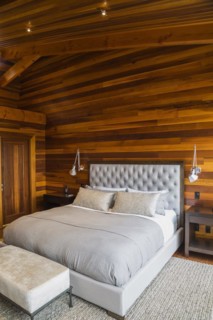 King size bed with grey upholstered panel headboard, ottoman and wooden end tables in master