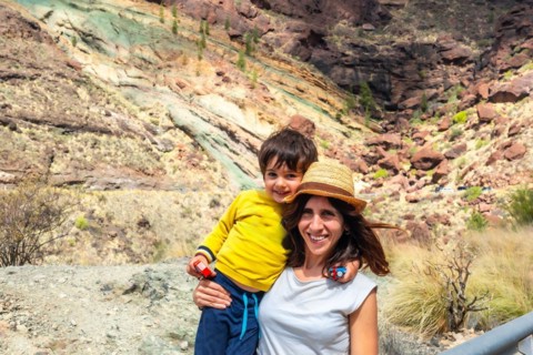 A woman and a child are posing for a picture in front of a rocky mountain. The woman is wearing a
