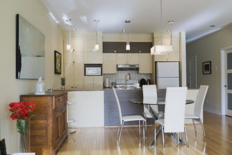 Dining room with round glass table, white leather high -back chairs and kitchen inside a renovated
