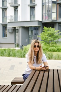 Woman called taxi using mobile application and is waiting for car while sitting on bench