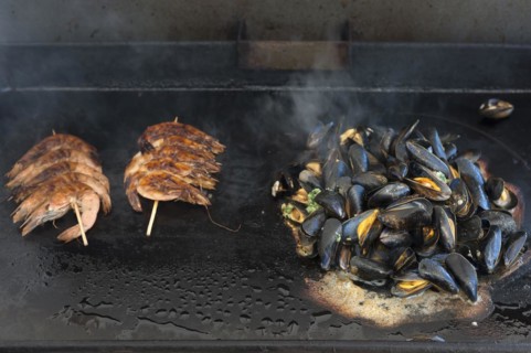 Mytilus (Mytilus edulis) are prepared on a gas barbecue on a plancha, left: prawns on a skewer,