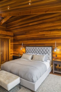 King size bed with grey upholstered panel headboard, ottoman and wooden end tables in master
