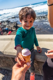 A young boy is holding an ice cream cone and giving it to another person. The scene is set on a