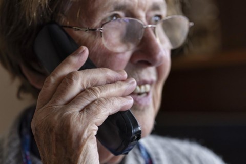 Laughing senior citizen with smock talking on the phone at home in her living room, Cologne, North