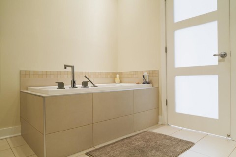 Soaking tub encased in a ceramic tile base in bathroom inside a renovated ground floor apartment in
