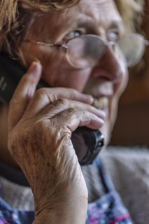 Laughing senior citizen with smock talking on the phone at home in her living room, Cologne, North