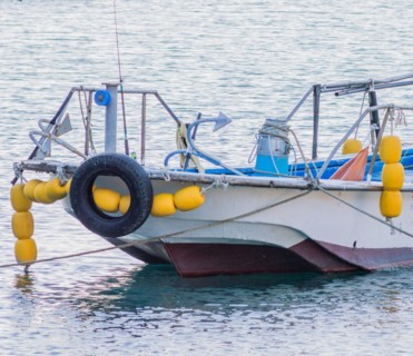Moored fishing boat with yellow buoys and a tire on calm blue sea waters, in South Korea