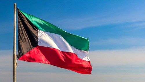 The flag of Kuwait flutters in the wind, isolated against a blue sky