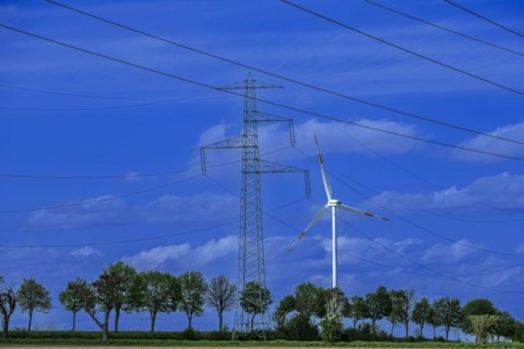 Electricity pylon with high-voltage lines and wind turbine on the K63 road with trees at the Avacon