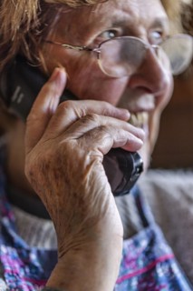 Laughing senior citizen with smock talking on the phone at home in her living room, Cologne, North