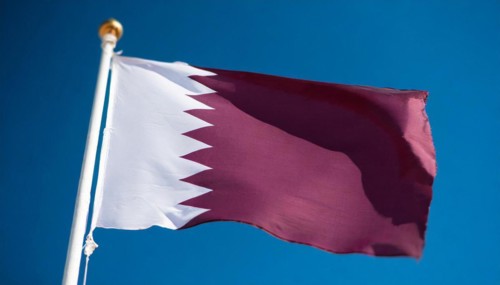 The flag of Qatar flutters in the wind, isolated against a blue sky