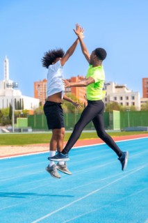 Vertical photo of two african american young friends jumping celebrating and clasping hands in a