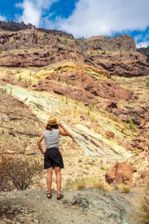 A woman with a hat at the Natural Monument Azulejos de Veneguera or Rainbow Rocks in Mogan, Gran