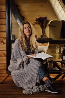 A woman wrapped in a plaid sits on the terrace in the evening and reads a book