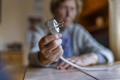 Senior citizen holding a power cable with plug in her hand at home, symbolising energy costs and