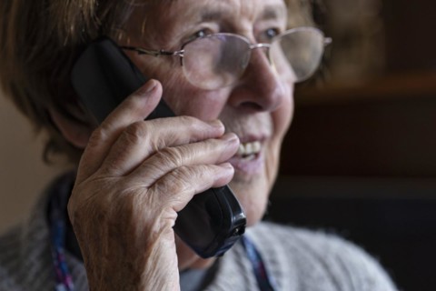 Laughing senior citizen with smock talking on the phone at home in her living room, Cologne, North