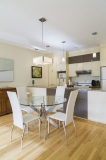 Dining room with round glass table, white leather high -back chairs and kitchen inside a renovated