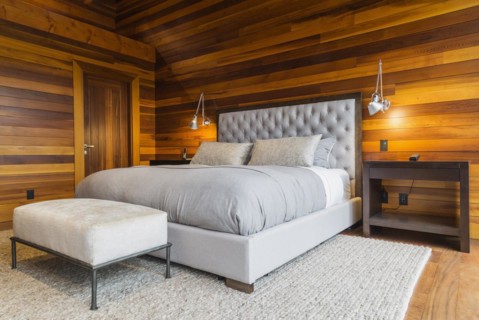 King size bed with grey upholstered panel headboard, ottoman and wooden end tables in master