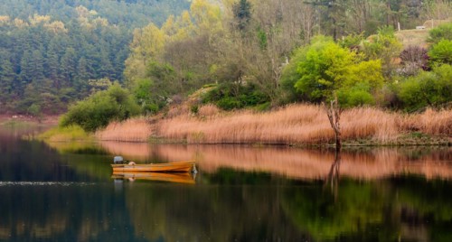 Small yellow metal fishing boat with small engine mount floating peacefully on a lake in South