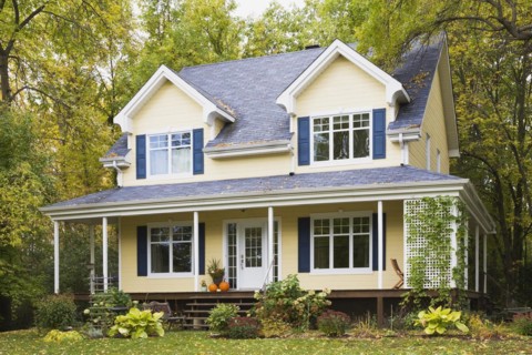 Two story yellow clapboard with blue and white trim cottage style home facade in autumn, Quebec,