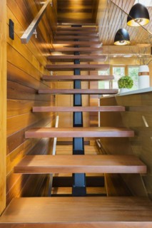 Looking up illuminated wooden staircase with opened steps and clear glass railing leading to
