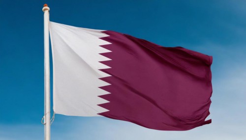 The flag of Qatar flutters in the wind, isolated against a blue sky