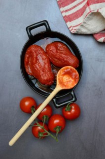 Whole tinned tomatoes in a pot, tomatoes and wooden spoon