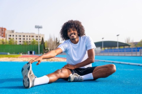 Frontal portrait of an African smiling man with curly hair and sports clothes stretching in an
