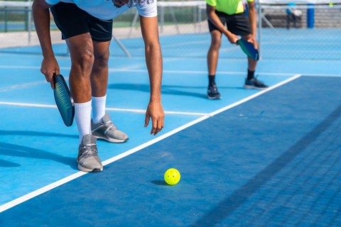 Cropped photo of the lower part of an african man bending to catch a pickleball ball from the floor