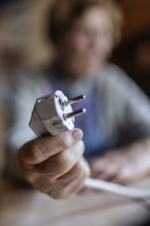 Senior citizen holding a power cable with plug in her hand at home, symbolising energy costs and