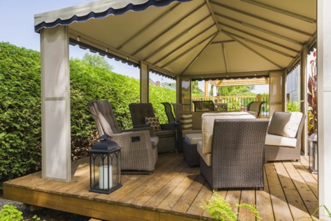 Gazebo on wooden deck furnished with wicker sitting chairs in backyard in summer, Quebec, Canada,