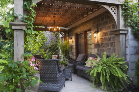 Rear of Renaissance grey stone and mortar castle style home with concrete patio and lattice covered