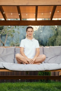 Cheerful woman sits cross-legged on a swing on backyard