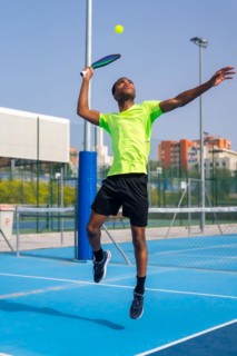 Vertical full length photo of an african man jumping to hit the ball playing pickleball outdoors