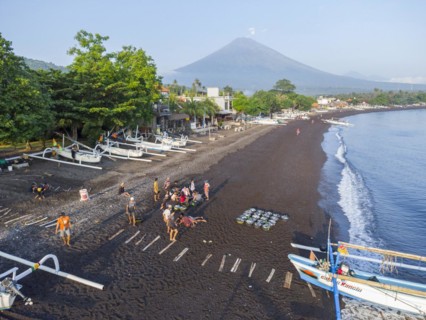 Fishermen unload their catch from their outrigger boat in the morning, in the background Gunung