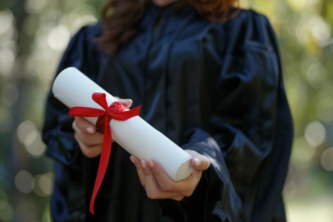 Woman in graduation robe holding degree paper certificate roll with red ribbon. KI generiert,