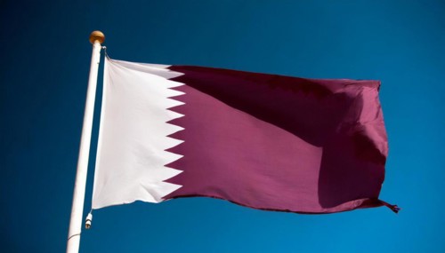 The flag of Qatar flutters in the wind, isolated against a blue sky