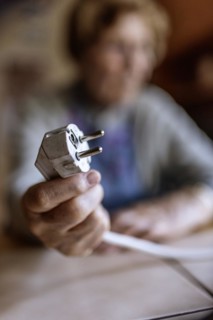 Senior citizen holding a power cable with plug in her hand at home, symbolising energy costs and